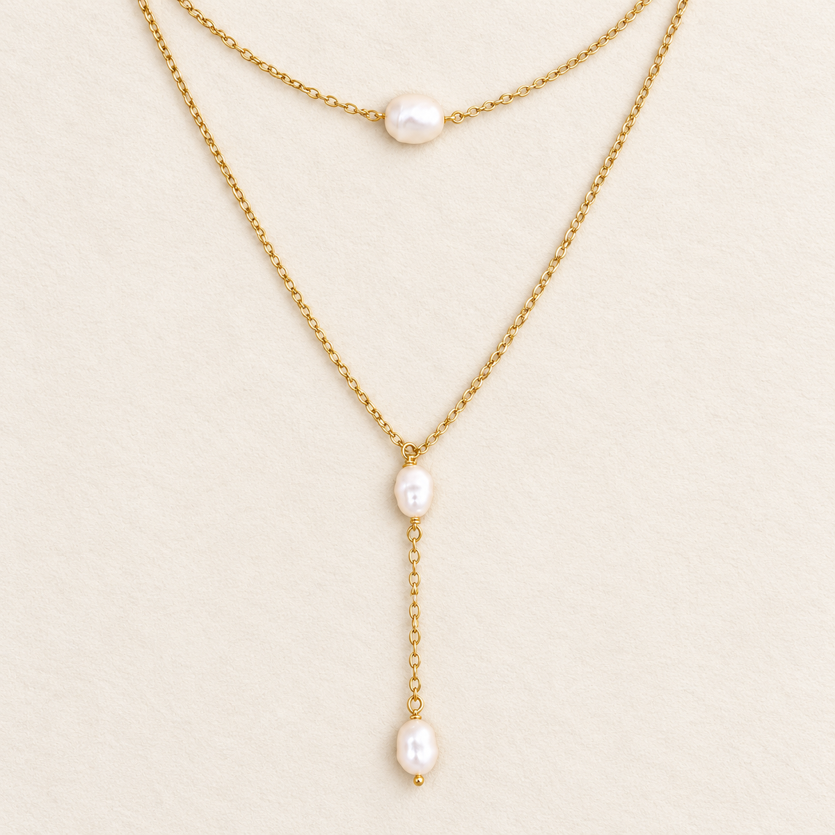 Pearl choker and lariat necklace set in 18k gold filled, both necklaces laid flat on a cream background
